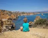 Kleinkind blickt auf die Küste Portugals. Felsen, türkisfarbenes Meer und eine Bucht mit Strand.