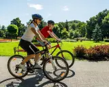 Dwie osoby na rowerach cieszą się piękną pogodą w parku. To pokazuje, co daje jazda na rowerze: aktywność, relaks i kontakt z naturą.