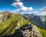 Malownicza trasa pieszo na Kasprowy Wierch. Kręta ścieżka wije się pośród zielonych zboczy Tatr, pod błękitnym niebem z chmurami.