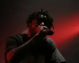 En 90 tals rappare med dreadlocks framför en röd ljusshow, svettig och fokuserad på mikrofonen.