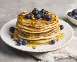 Stapel fluffiger High Protein Pancakes mit Blaubeeren und Mandelsplittern, beträufelt mit Honig.