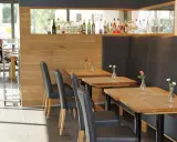 Mesas de madera con floreros y sillas negras en un restaurante. La distancia entre mesas permite un espacio cómodo.