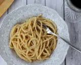 Porcja pysznego cacio e pepe na ozdobnym talerzu, z widelcem w makaronie.