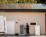 En tekniker installerar ett batterilager för dt energi vid ett hus med solpaneler på taket.