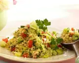 Frischer Couscous-Salat mit Tomaten, Gurken und Kräutern, garniert mit Petersilie. Ein Löffel voller Genuss.