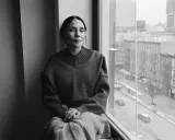 Ming Smith, a woman with her hair pulled back, sits by a window, looking out at a city street.
