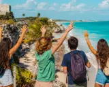 Cuatro jóvenes con mochilas saludan al mar turquesa y las ruinas mayas. ¡Una aventura inolvidable en la Riviera Maya con niños!