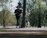 En ung kvinna och hennes hund springer längs en stig i en park. De njuter av våren och frisk luft.