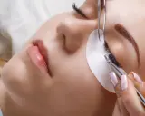 Une esthéticienne utilise des pinces pour appliquer des extensions de cils, une étape clé pour savoir comment coiffer ses sourcils et sublimer le regard.