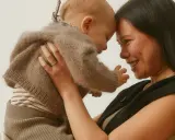 Madre y bebé se miran con ternura, frente con frente. El bebé, envuelto en un suéter de lana, muestra el apego infantil.