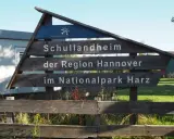 Drewniany drogowskaz "Schullandheim der Region Hannover im Nationalpark Harz" zapowiada przygodę w górach w Niemczech, być może z widokiem na szczyt Brocken.
