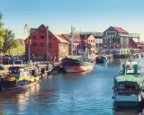 Barche ormeggiate nel porto di Klaipeda, Lituania, con edifici storici e gru sullo sfondo.
