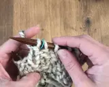 Manos tejiendo con agujas de madera un punto de relieve con lana gruesa y un marcador azul.