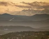 Widok na Tatry z Krakowa. Samolot leci nad mglistymi wzgórzami, a za nimi widać ośnieżone szczyty.