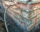 Naprawa pękania ścian w narożnikach. Widać zbrojenie i wąż doprowadzający zaprawę.