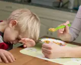 Dziecko z brakiem apetytu, sennością i zmęczeniem odwraca głowę od jedzenia. Mama próbuje nakarmić go łyżeczką.