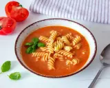 A miseczce zupy pomidorowej z makaronem fusilli, listkami bazylii i połówkami pomidorów obok. Idealne przyprawy do zupy pomidorowej.