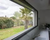 Vista desde una cocina moderna con **ventanas automáticas** que enmarcan un jardín con palmera y vegetación frondosa.