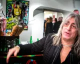Mikkey Dee son, en man med långt grått hår och en silverfärgad kedja, poserar vid ett bord med blommor och flaskor.