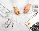 Manos de arquitecto dibujando planos, con calculadora, laptop y bocetos. El significado de "as built" se refleja en la precisión del diseño.
