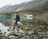 Kobieta z plecakiem przemierza kamieniste brzegi górskiego jeziora. W tle skaliste zbocza, idealne dla skandynawskie marki outdoorowe.