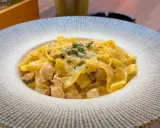 Pyszny makaron włoski z kawałkami kurczaka w kremowym sosie, posypany ziołami i parmezanem.