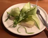 En läcker pilgrimsmussla med gurka och salladslök, serverad på en tallrik i en mysig wood restaurang.
