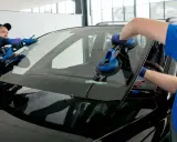 Dwóch mechaników wymienia szybę samochodową za pomocą przyssawek.