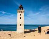 Ett vitt utsiktstorn i Danmark reser sig mot en blå himmel. Sanddyner och hav omger tornet.