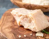 Kawałek twardego sera, przypominającego Grana Padano i parmezan, leży na drewnianej desce.