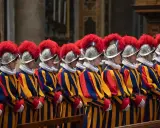 Guardia svizzera pontificia in divisa storica, con elmi piumati e abiti a righe blu, gialle e rosse, in posa solenne.