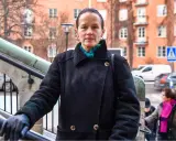 Malin Berghagen, trots att hon verkar sjuk, går uppför en trappa i en svart kappa.