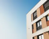 Façade d'un immeuble moderne avec balcons et volets roulants, idéal pour mettre son appartement en location. Ciel bleu clair.