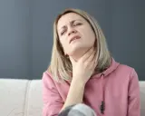 Kobieta z bólem szyi, próbująca ćwiczenia na porażenie fałdu głosowego.
