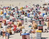 Bunte Strandkörbe säumen den Sandstrand, einige Menschen entspannen sich, andere spielen Volleyball. Ein typischer fkk strand.