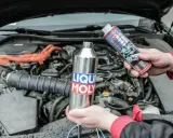 Ręce trzymające preparaty Liqui Moly do czyszczenia katalizatora. W tle widać silnik samochodu.
