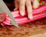 Eine Hand schneidet mit einem Messer die roten Stiele von Mangold, um ihn zuzubereiten.