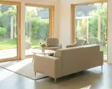 Salón moderno con grandes ventanales que dan a un jardín. Muebles claros y minimalistas. Ideal para aprovechar la luz natural y las deducciones IRPF por eficiencia energética.