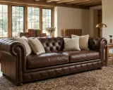 Brun Chesterfield-soffa i anilin skinn med knappad rygg och armstöd. Prydnadskuddar och en antik matta ger en varm känsla.