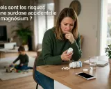 Besorgte Frau liest Beipackzettel einer Magnesium-Dosierung. Ein Kind spielt im Hintergrund.