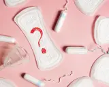Pytajnik z krwi na podpaskach, obok tampony i kubeczek menstruacyjny. Czy to plamienie przed okresem?