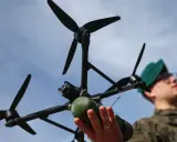 Młody dron wiek. Żołnierz w zielonym beretcie trzyma w dłoniach nowoczesny dron z kamerą i zielonym ładunkiem.