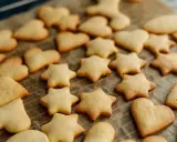 Upieczone ciasteczka z foremek w kształcie gwiazdek i serduszek leżą na papierze do pieczenia.