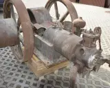 Zardzewiały silnik na gaz drzewny, z dużymi kołami, stoi na drewnianych klockach.