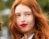 Eine Frau mit leuchtend roter haarfärbung und roten Lippen, ihr Haar weht im Wind.