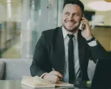 Uśmiechnięty mężczyzna w garniturze rozmawia przez telefon, notując coś w zeszycie. To właśnie taki mikroprzedsiębiorca buduje swój biznes.