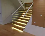 Nowoczesne schody dywanowe na beton z podświetleniem LED. Szklana balustrada i drewniane stopnie tworzą elegancką całość.