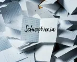 Rozrzucone kartki w kratkę, na jednej napis "Schizophrenia". Obraz symbolizuje chaos myśli, objawy schizofrenii hebefrenicznej.