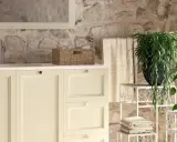 Bagni rustici di campagna con mobile lavabo color crema, cesto in vimini, piante verdi e pareti in pietra grezza.