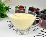 A glass boat filled with smooth, creamy krem angielski, ready to be poured over fresh berries in jars.